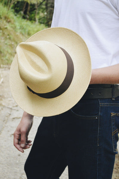 Man in white T Shirt and Blue jeans holding a classic natural Panama hat with a dark band